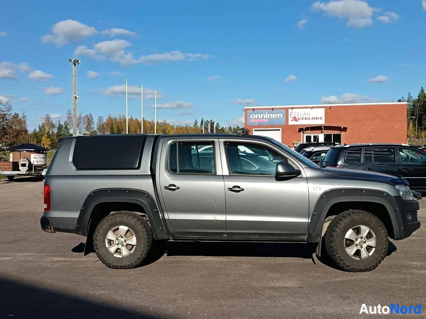 Etuviisto, nokka oikealle: Harmaa Volkswagen Amarok -lisävarustekuormatila sivukulmasta, korostetut mustat levikeharjat.