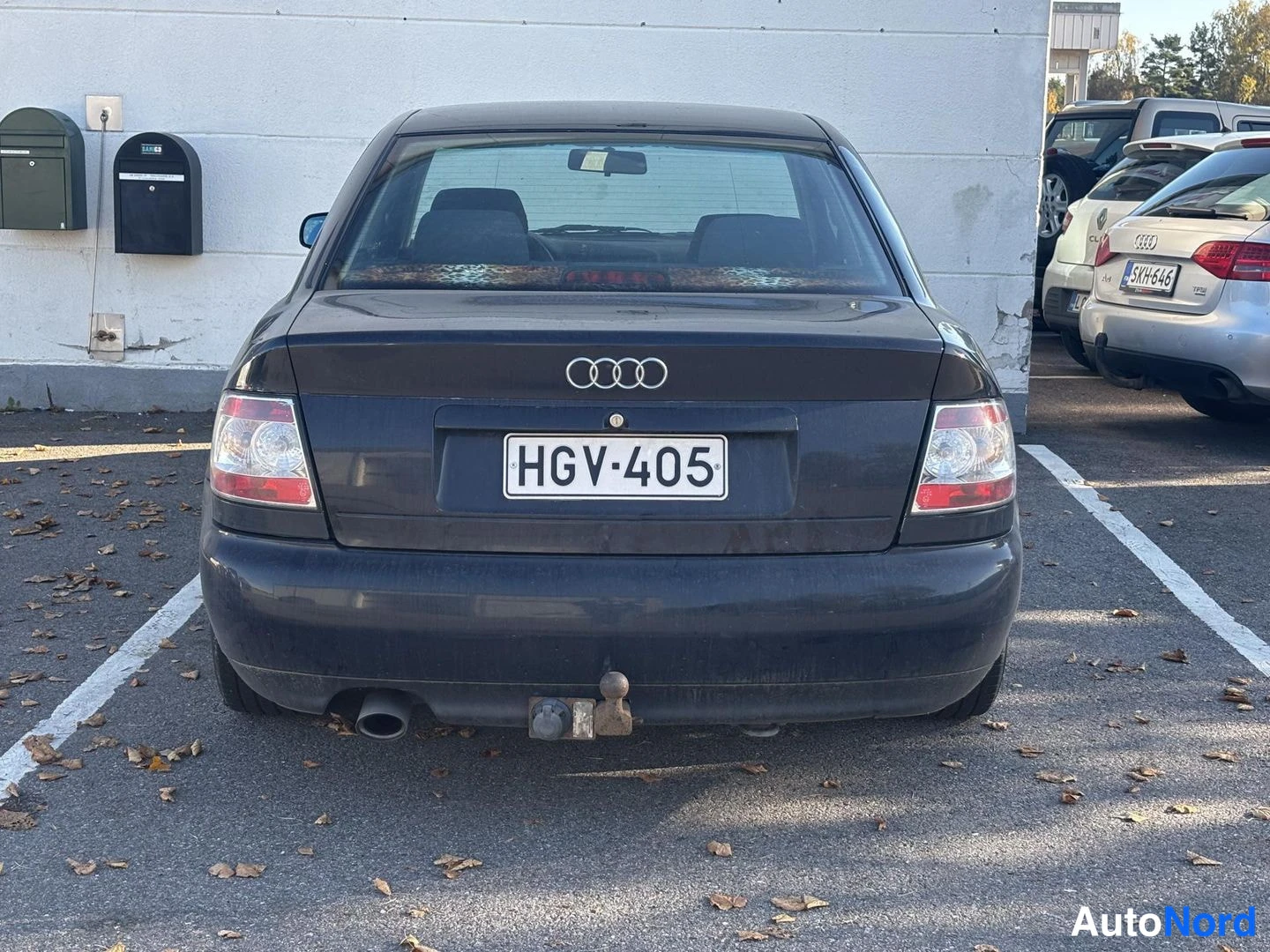 Takaa: Auton takaosa suoraan takaa: tumma Audi-sedan, rekisteritunnus, takana njäksi asennettu vetokoukku ja vasemmalla pakoputki.
