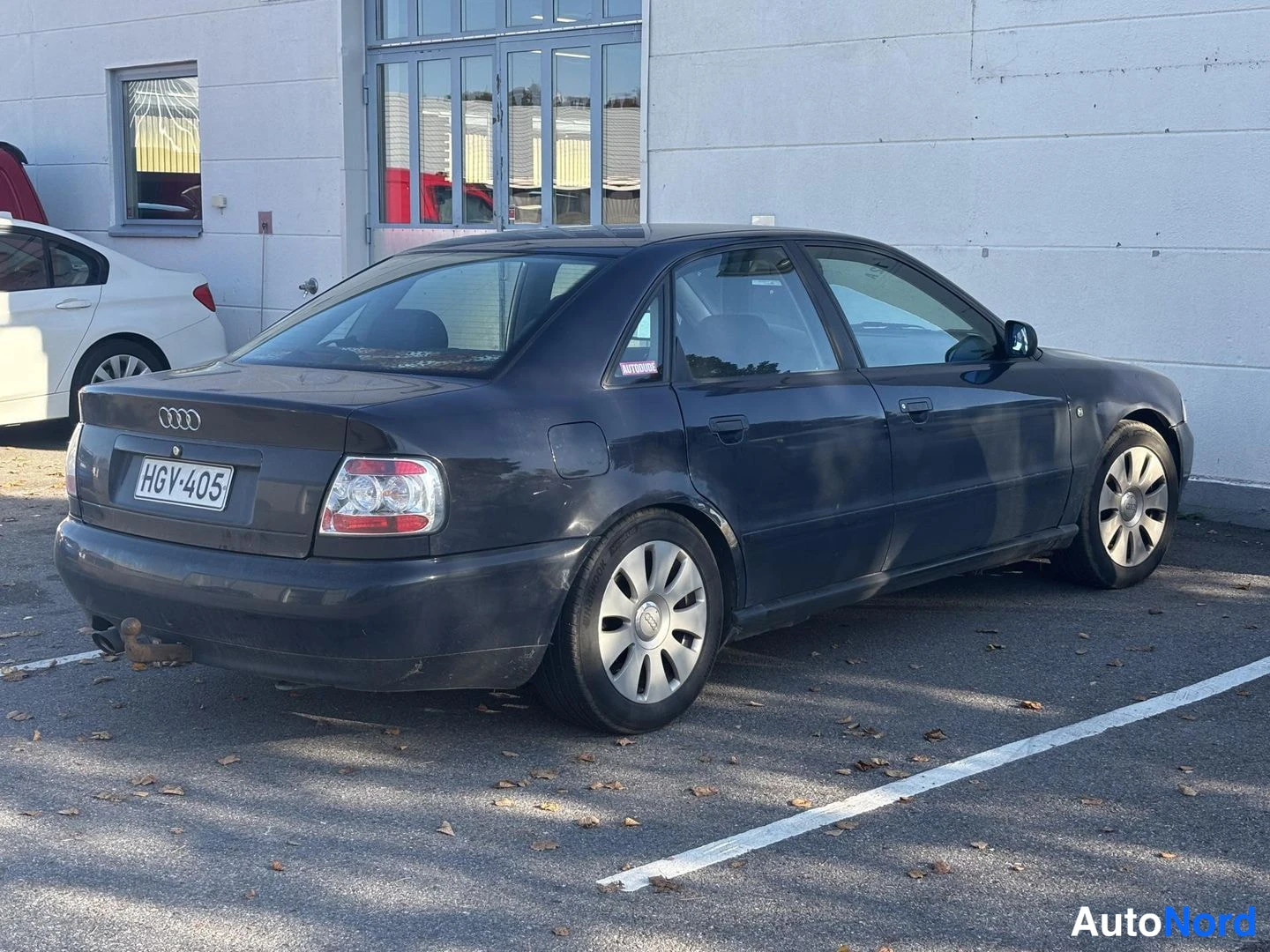 Takaviisto: Taka- ja sivukulmassa kuvattu tumma neliovinen Audi-sedan, rekisteritunnus, hopeanvalkoisilla kevytmetallivanteilla parkkipaikalla.