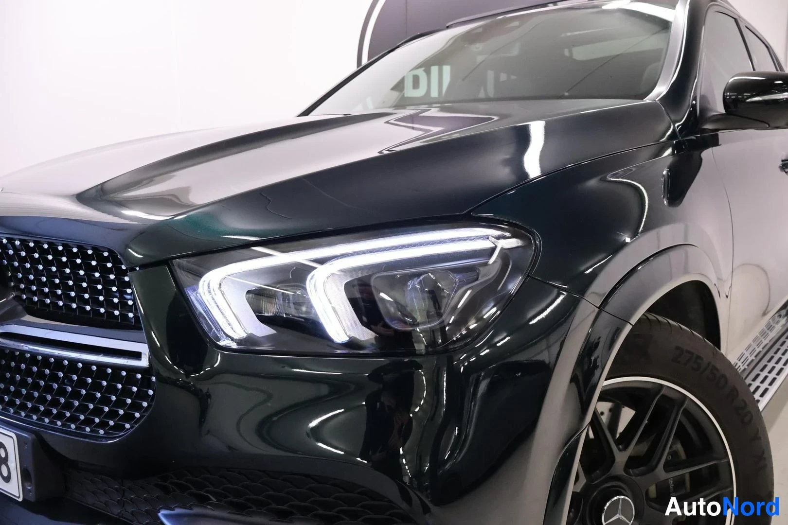 Edestä: Tarkku kuva Mercedes-Benz GLE:n etupäästä: kesävalo ja kyljistyvä nokka mustanvihreällä korilla.