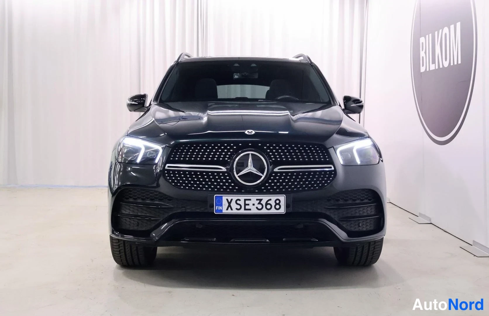 Edestä: Mustanvihreän Mercedes-Benz GLE:n etupää suoraan edestä; näkyvissä tähtitunnuksella varustettu pystysäleikkö, LED-ajovalot ja rekisterikilpi.