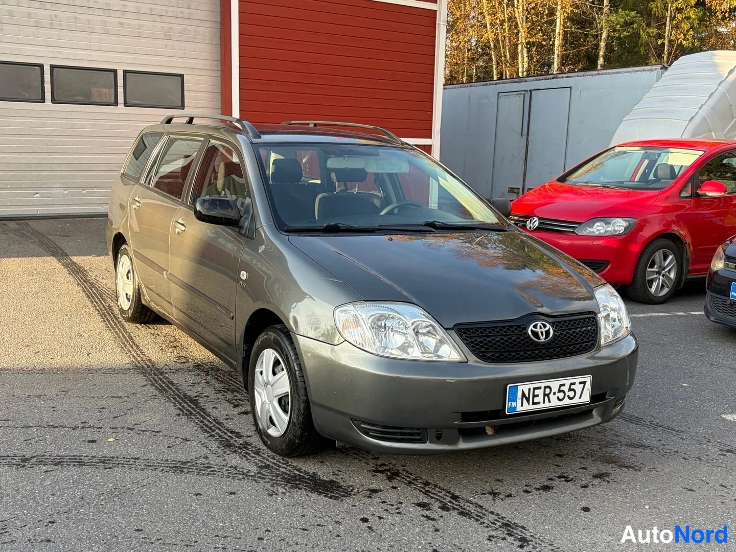 Etuviisto, nokka oikealle: Tummanharmaa Toyota Corolla -farmari edessä oikealta kolmannelta kuvattuna; etusäleikkö ja kylki näkyvät, EU-merkintä, kattotelineet.