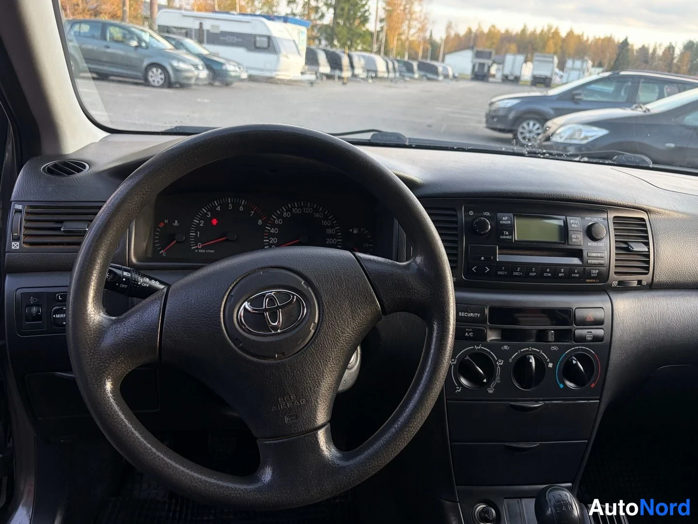 Muu: Näkymä ohjauspyörään ja kojetauluun: Toyota-emblem, analogiset nopeus- ja kierrosmittarit, radio- ja ilmastointia säätimet, A/C-nappi.