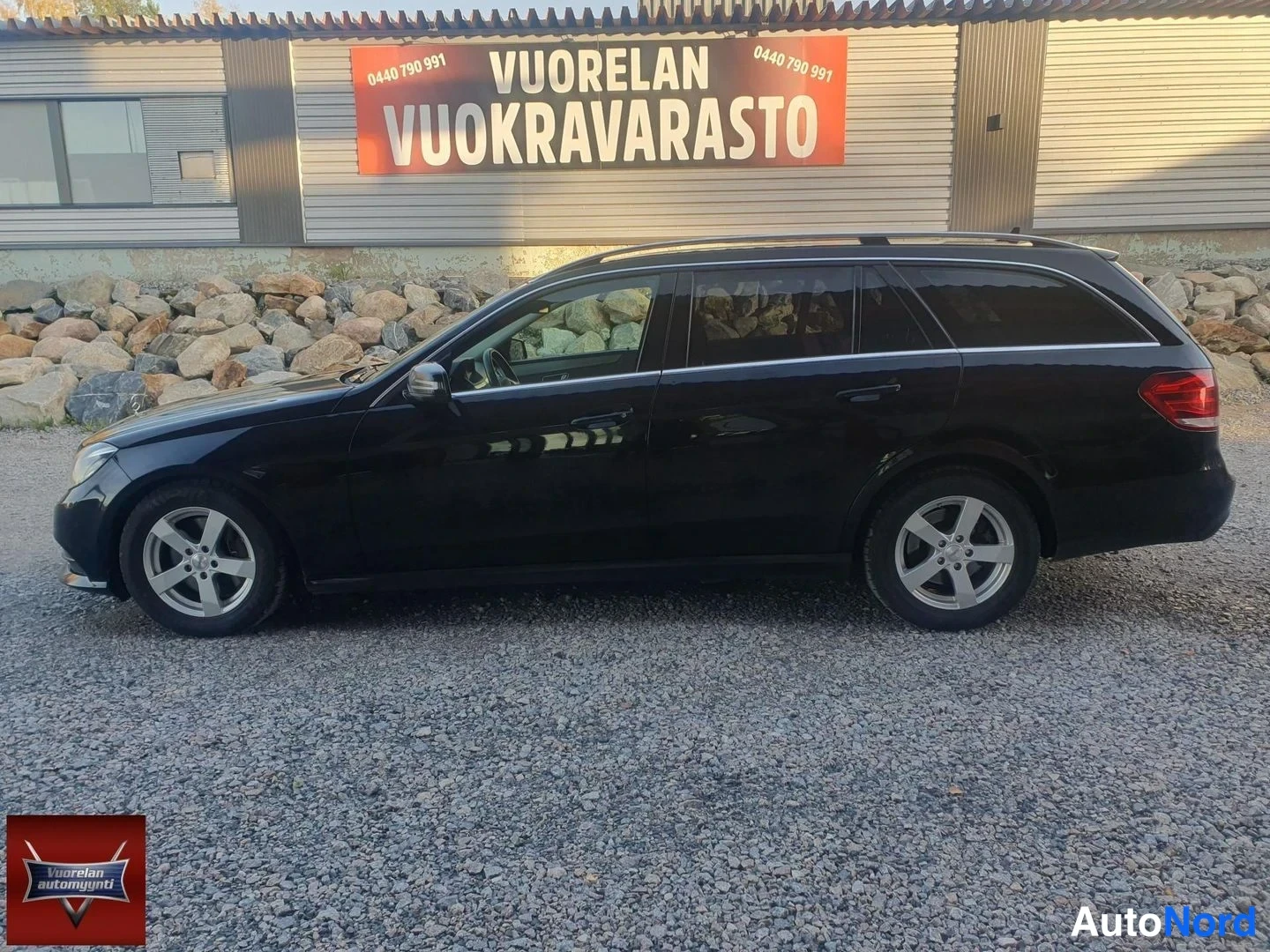 Takaviisto: Mustan farmariautin sivutakakulma sorapihalla; takavalot, takapuskuri ja kattokaaret näkyvät, taustalla vuokravarastokyltti.