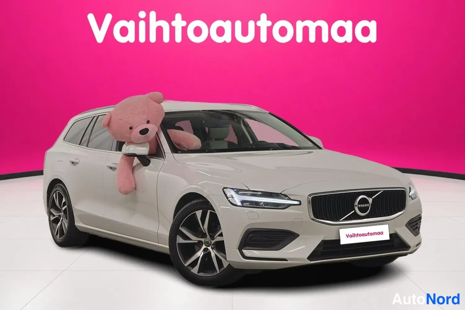 Etuviisto, nokka oikealle: Volvo V60 -farmariauto valkoisena etukulmasta oikealta, etusälekori ja kylki näkyvissä, pehmolelu takana