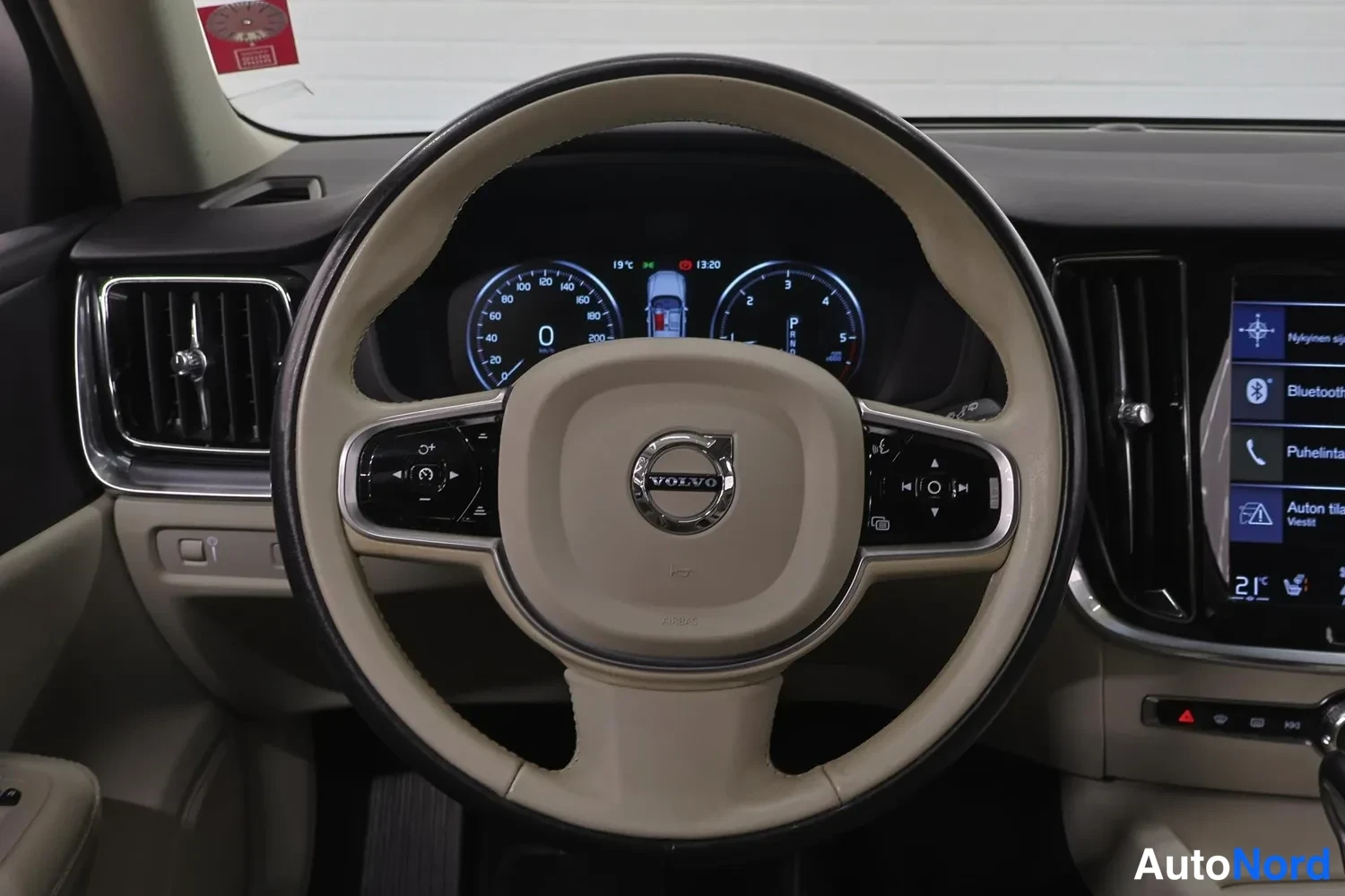 Yksityiskohta: Lähikuva beige Volvo-ohjauspyörästä ja digitaalisesta mittaristosta, jossa näkyy kirjain P (PARKED).