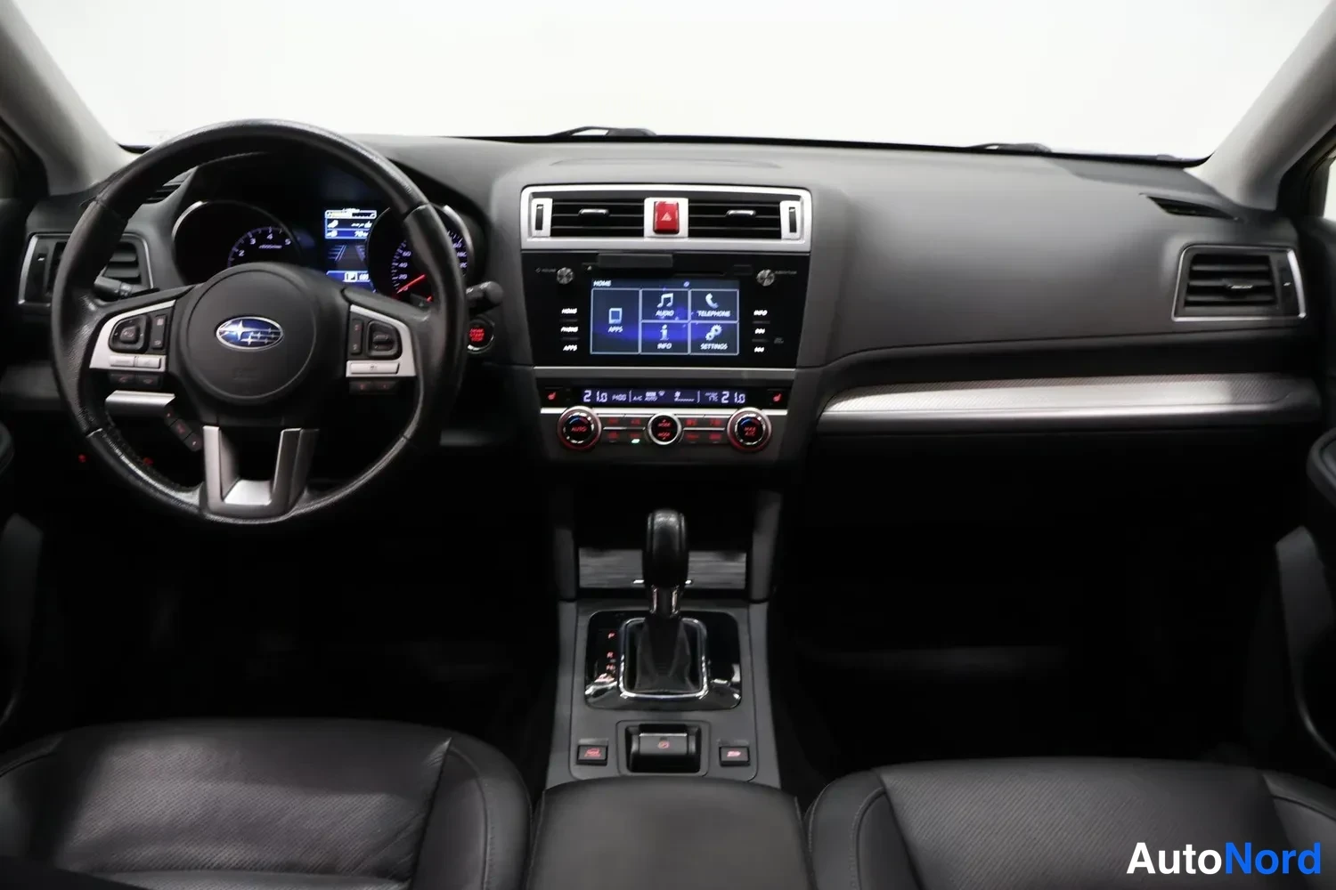 Edestä: Ohjaamo suoraan edestä: Subaru-ohjauspyörä, kojelauta, kosketusnäyttö ja automaattivaihteen valitsin, mustat istuimet.