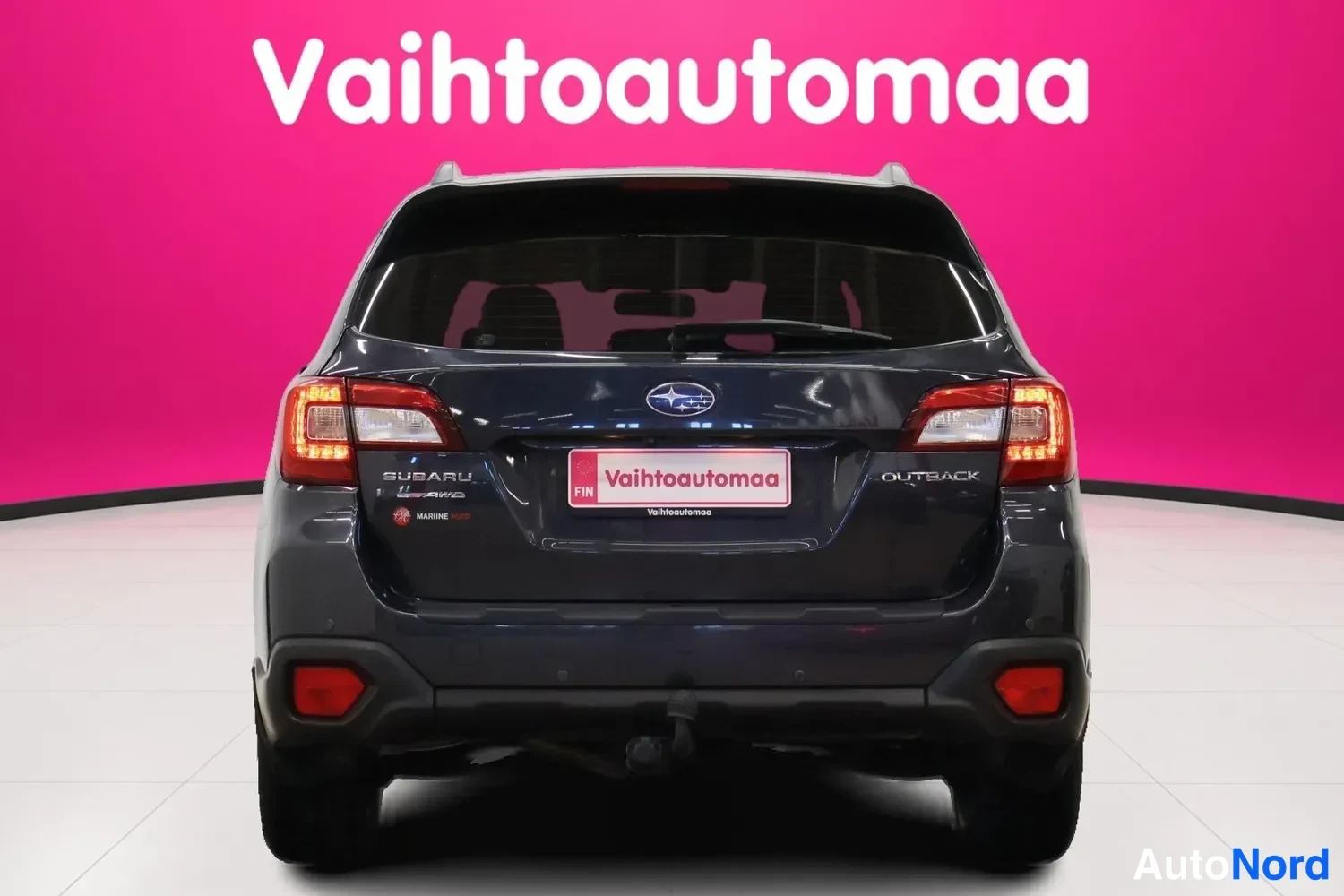 Takaa: Subarun takaa näkyvät takavalot, SUBARU- ja OUTBACK-merkit sekä Vaihtoautoma-kilpi tummansinisessä farmarissa.