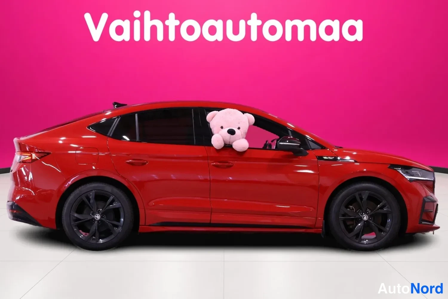 Etuviisto, nokka oikealle: Punainen henkilöauto sivuprofiilista, etuvalo oikealla ja perä vasemmalla; pehmolelu ikkunassa.