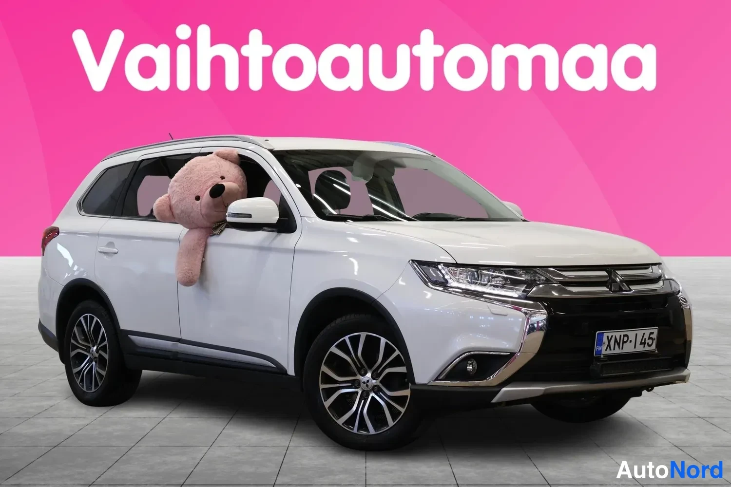 Etuviisto, nokka oikealle: Valkoinen Mitsubishi Outlander etuviistossa oikealta, rekisteritunnus, pehmolelu näkyy etuikkunassa.