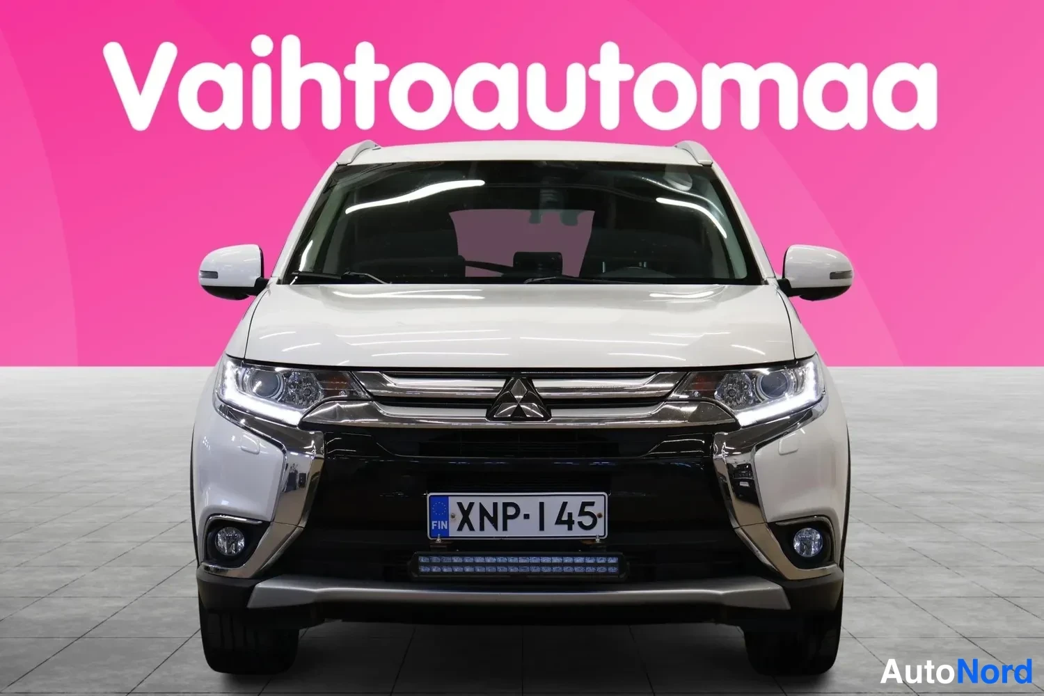 Edestä: Valkoisen Mitsubishi Outlanderin etunäkymä, rekisteritunnus, apuvalot puskurissa.