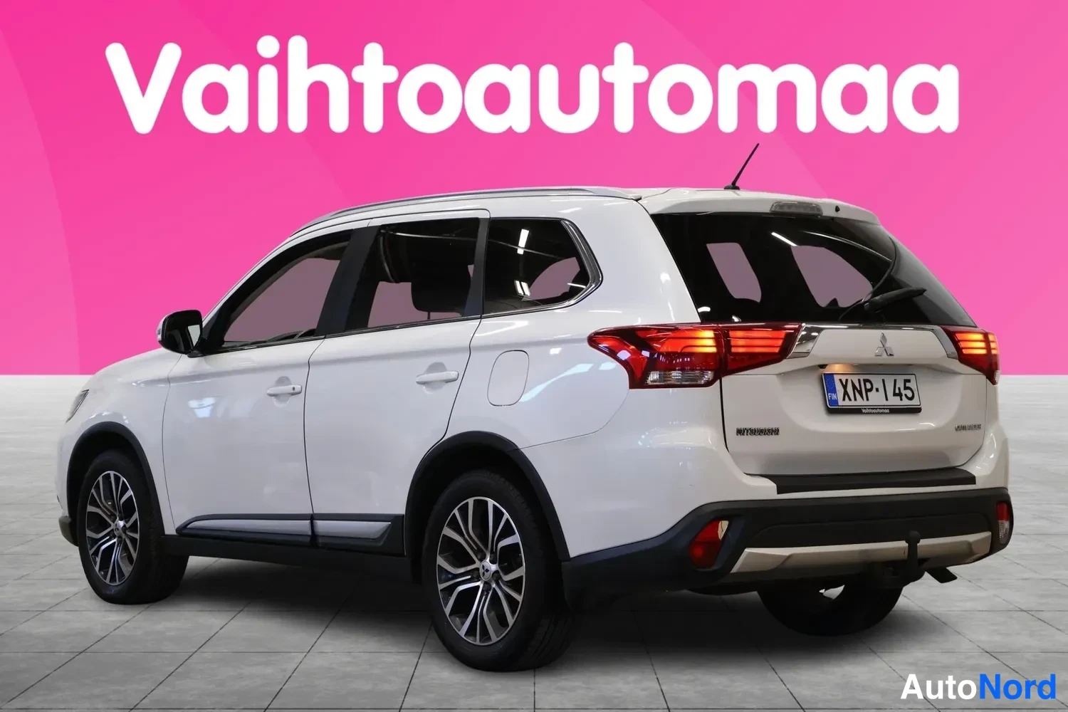 Takaviisto: Valkoinen Mitsubishi Outlander takaa oikealta kulmasta nähtynä, rekisterikilpi ja vetokoukku näkyvissä.