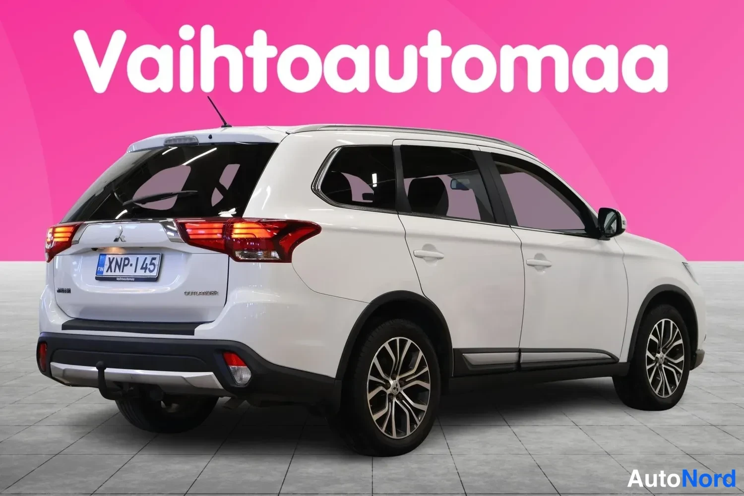 Takaviisto: Valkoinen Mitsubishi Outlander takaa oikealta kolmesta neljäsosasta nähtynä, rekisterikilpi ja vetokoukku.