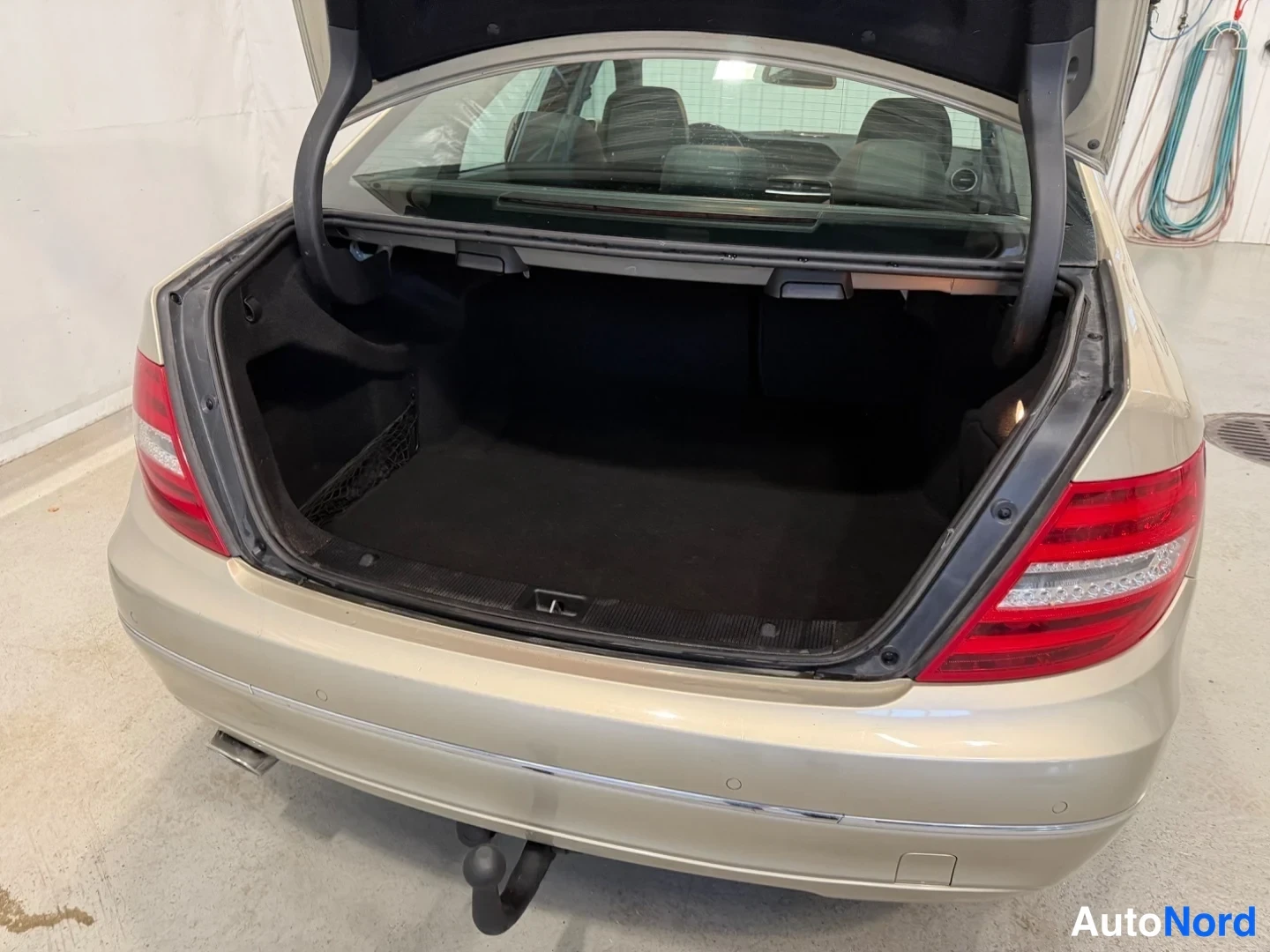 Takaa: Mercedes-Benz C-sedanin avattu tavaratila takaa kuvattuna, kansi ylhäällä ja metallihaken kiinnitetty.