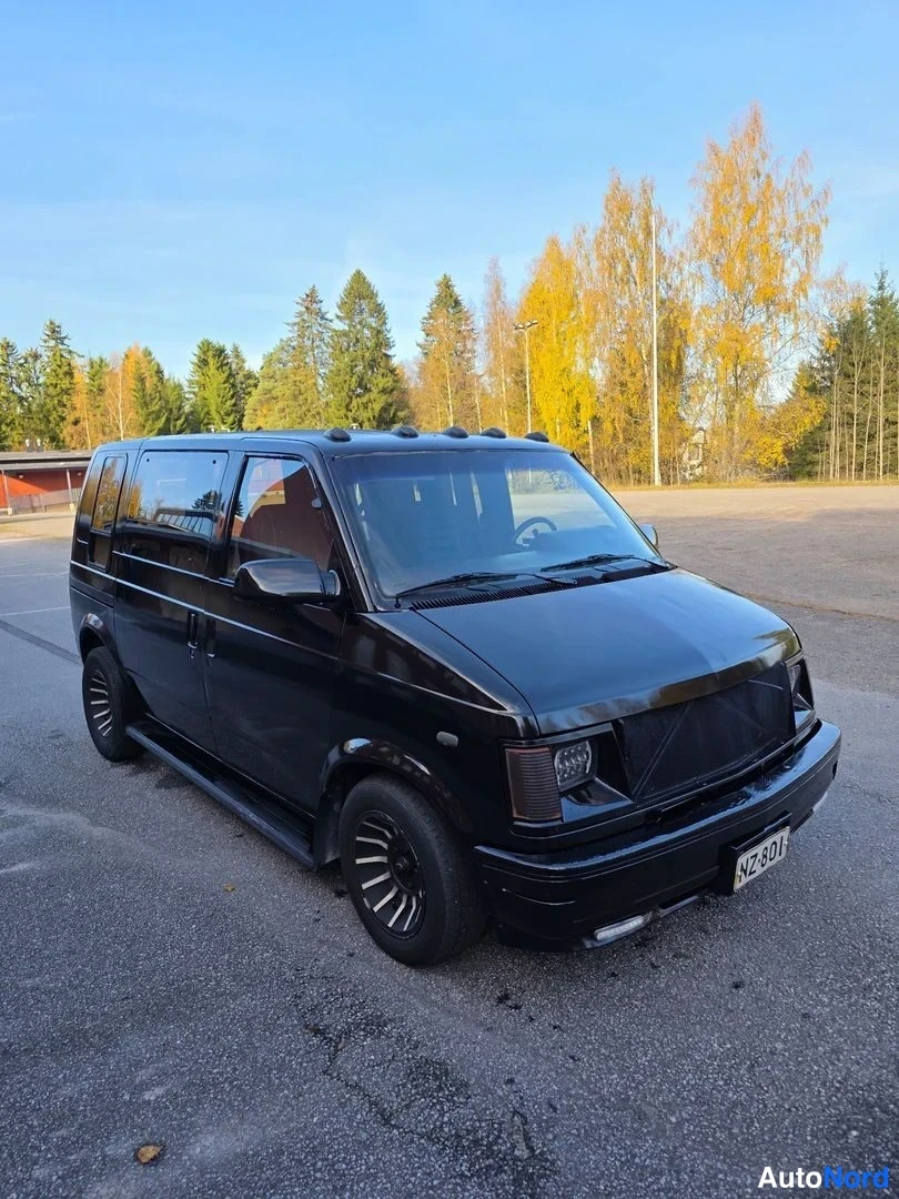 Etuviisto, nokka oikealle: Musta Chevrolet Astro -pakettiauto kulmassa etu-oikealta kuvattuna, etusäleikkö ja ajovalot näkyvät, rekisterikilpi NZ-801.