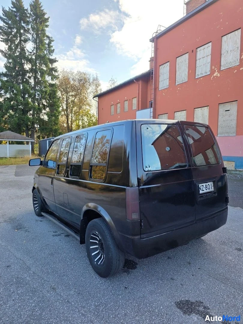 Takaviisto: Mustan Chevrolet Astro -pakettiauton takaosa ja sivu kuvattuna takaa punaisen rakennuksen edessä, rekisterikilpi NZ-801.