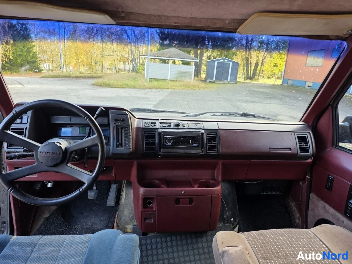 Muu: Kojelauta suoraan edestä: ohjauspyörä Chevrolet-tekstillä, JVC-radio, kupitelineet, ruskeapunainen panelointi.
