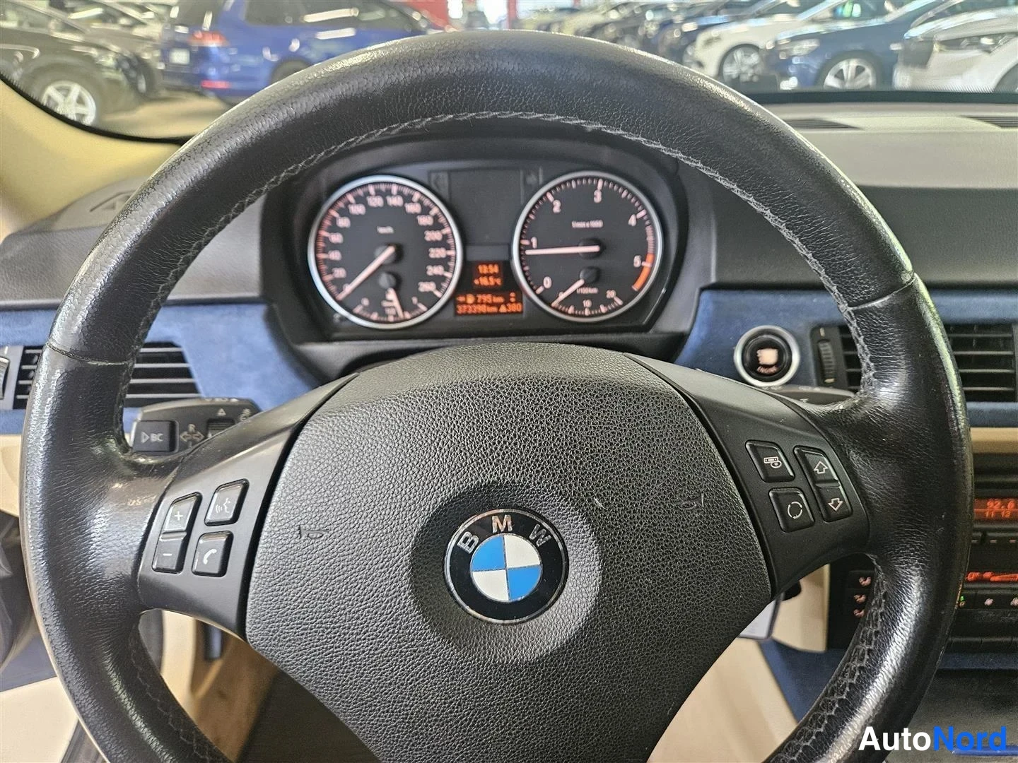 Yksityiskohta: Ohjauspyörän ja kojelaudan lähikuva: BMW-merkillä varustettu ohjauspyörä, mittaristo ja monitoiminapit näkyvät.
