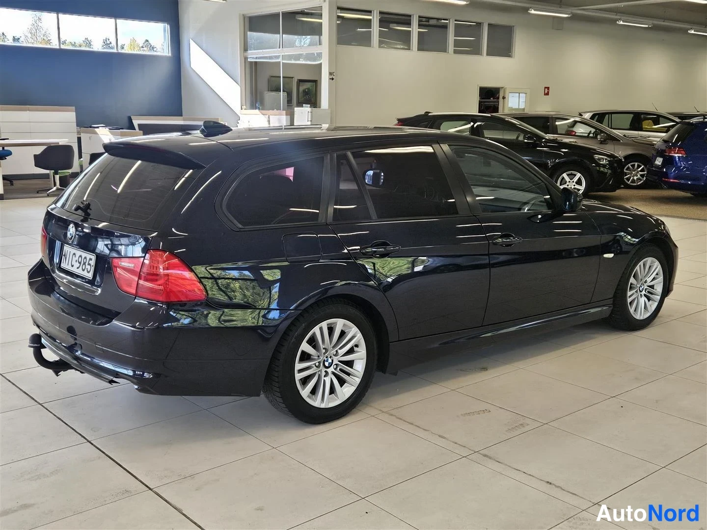 Takaviisto: Tumma BMW-farmari takaviistosta oikealta, rekisteritunnus, vetokoulu näkyvissä.
