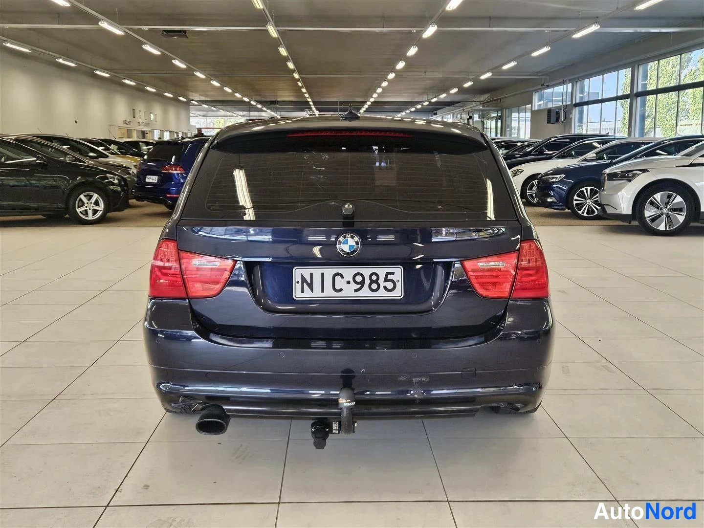 Takaa: Tumman sinertävän musta BMW-farmari suoraan takaa, rekisteritunnus, vetokoulu ja pakoputki näkyvissä.