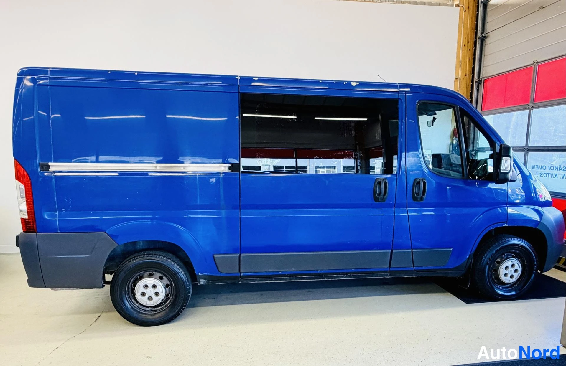 Sivulta: Sivulta kuvattu sininen pakettiauto, jonka takaa- ja sivulasi on tummennettu.