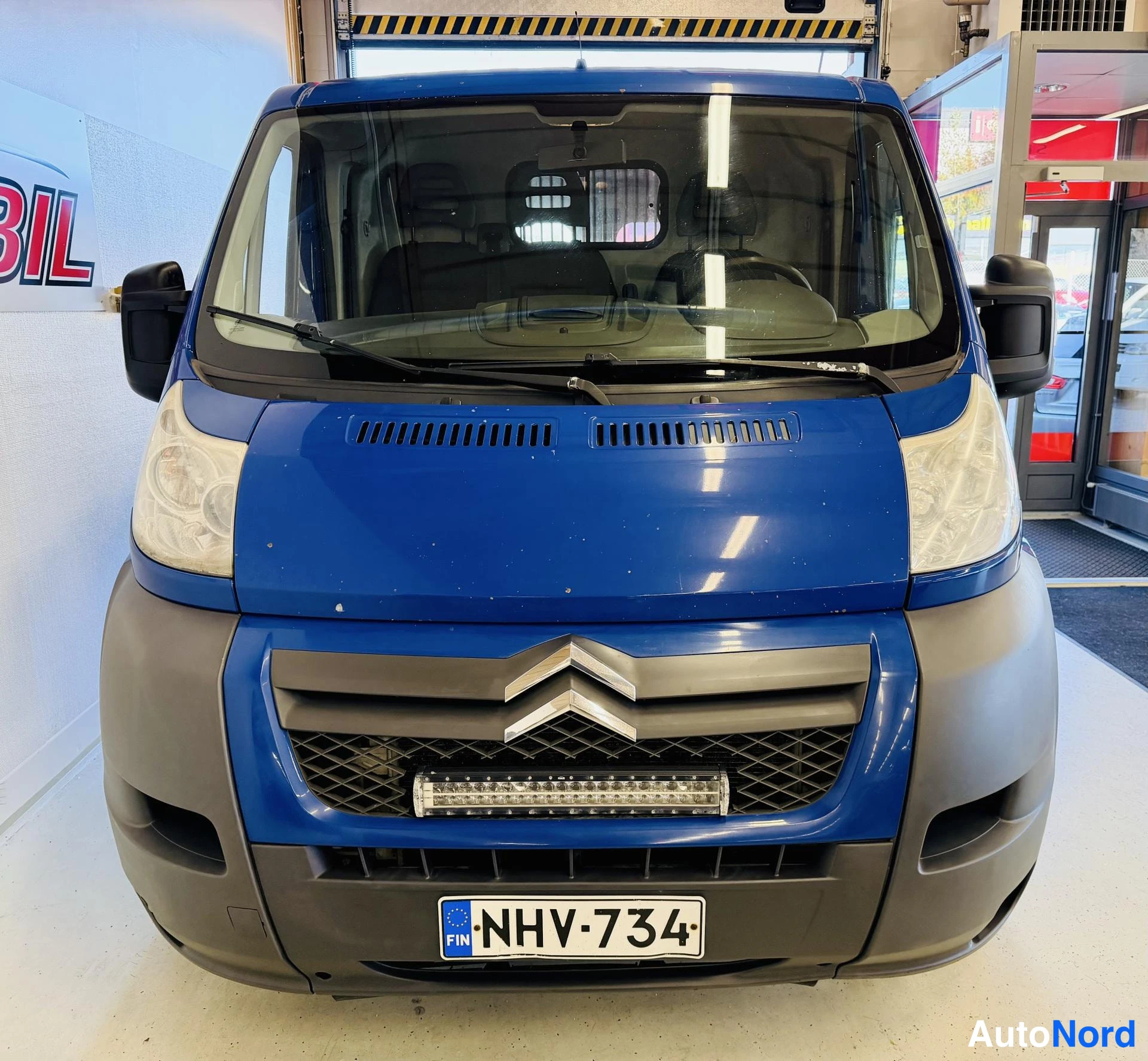 Edestä: Sininen pakettiauto edestä kuvattuna; konepellissä Citroënin logo ja rekisterikilpi.