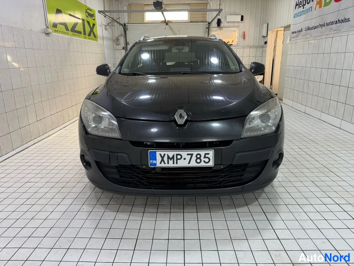 Edestä: Renault Megane -farmarin etupään suorakuva tummassa värisävyssä, rekisterikilpi.