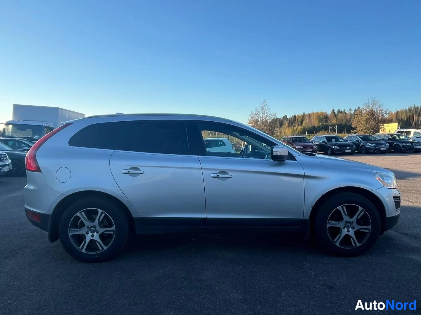 Sivulta: Hopeanvärinen Volvo XC60:n sivuprofiili oikealta puolen, parkkipaikalla taivaansininen taivas.