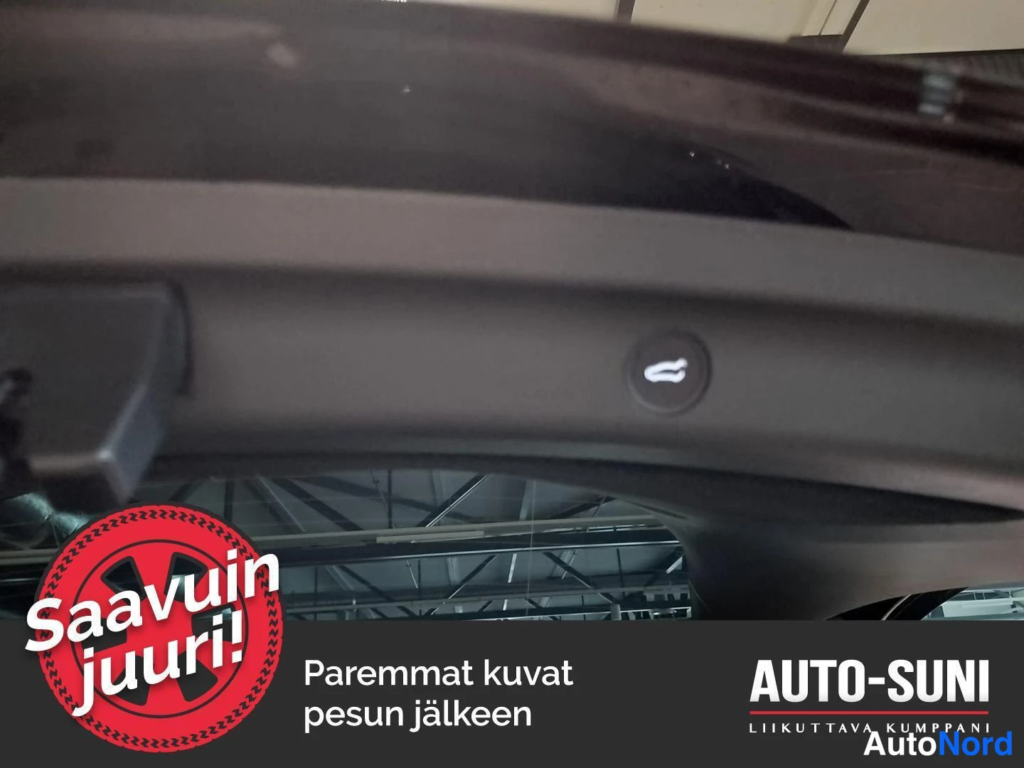 Yksityiskohta: Sisäkuva takaluukun aukaisupainikkeesta mustassa paneelissa; mahtaa tekstit Saavuin juuri ja Auto-Suni.