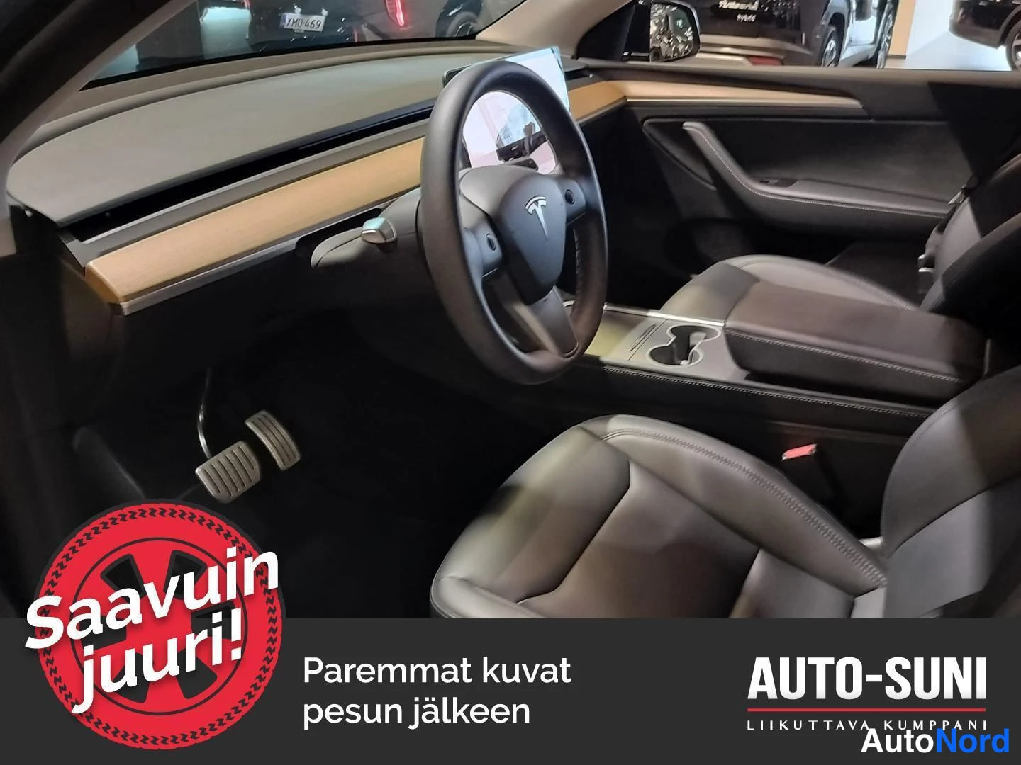 Muu: Auton ohjaamo vasemmalta eteenpäin kuvattuna: Tesla-merkkinen ohjauspyörä, tummat penkit ja keskikäytävän kupitelineet.