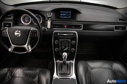 Muu: Volvo V70:n ohjaamo edestä kuvattuna: Volvo-merkkinen ohjauspyörä, mittaristo, keskinäytön infotainment, automaattivaihteen valitsin ja keskikonsolin säätimet.