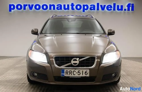 Edestä: Auton etunäkymä suoraan edestä, ruskea Volvo rekisterillä valot päällä hallissa.