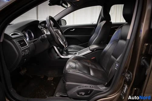 Muu: Volvo V70:n etuistuimet ja ohjaamo kuljettajanoven aukiosta kuvattuna; mustat nahkaiset istuimet, ratin ja kojelaudan osia näkyvissä.