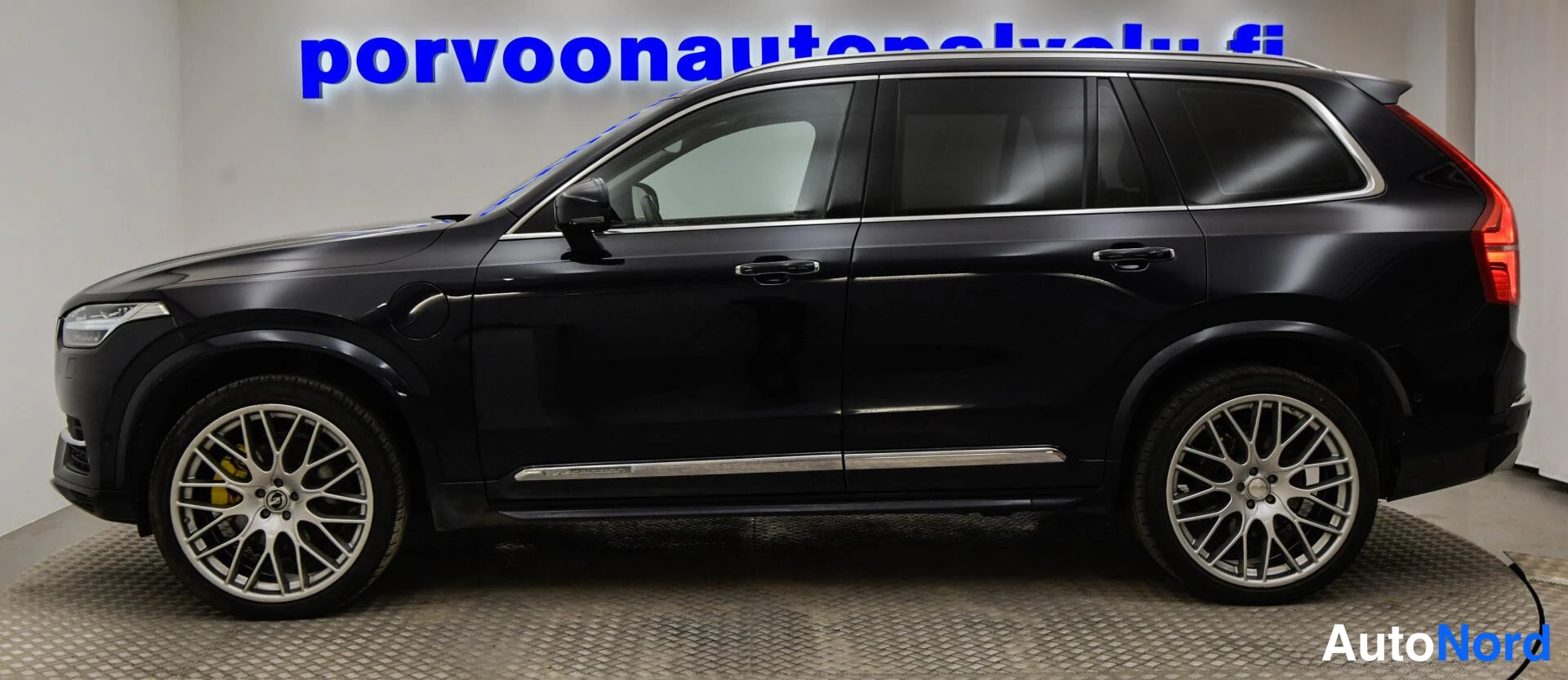Sivulta: Sivunäkymä tummasta Volvo XC90 -maasturista, vaaleat vanteet ja kromilista ovien alapuolella.