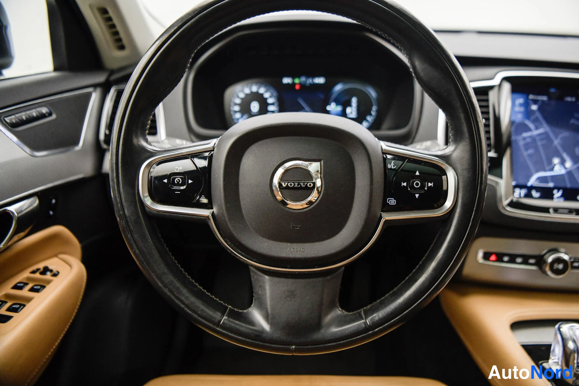Muu: Volvo-logolla varustettu ohjauspyörä lähikuvassa, kojelaudan mittaristo ja osa näytöstä taustalla.