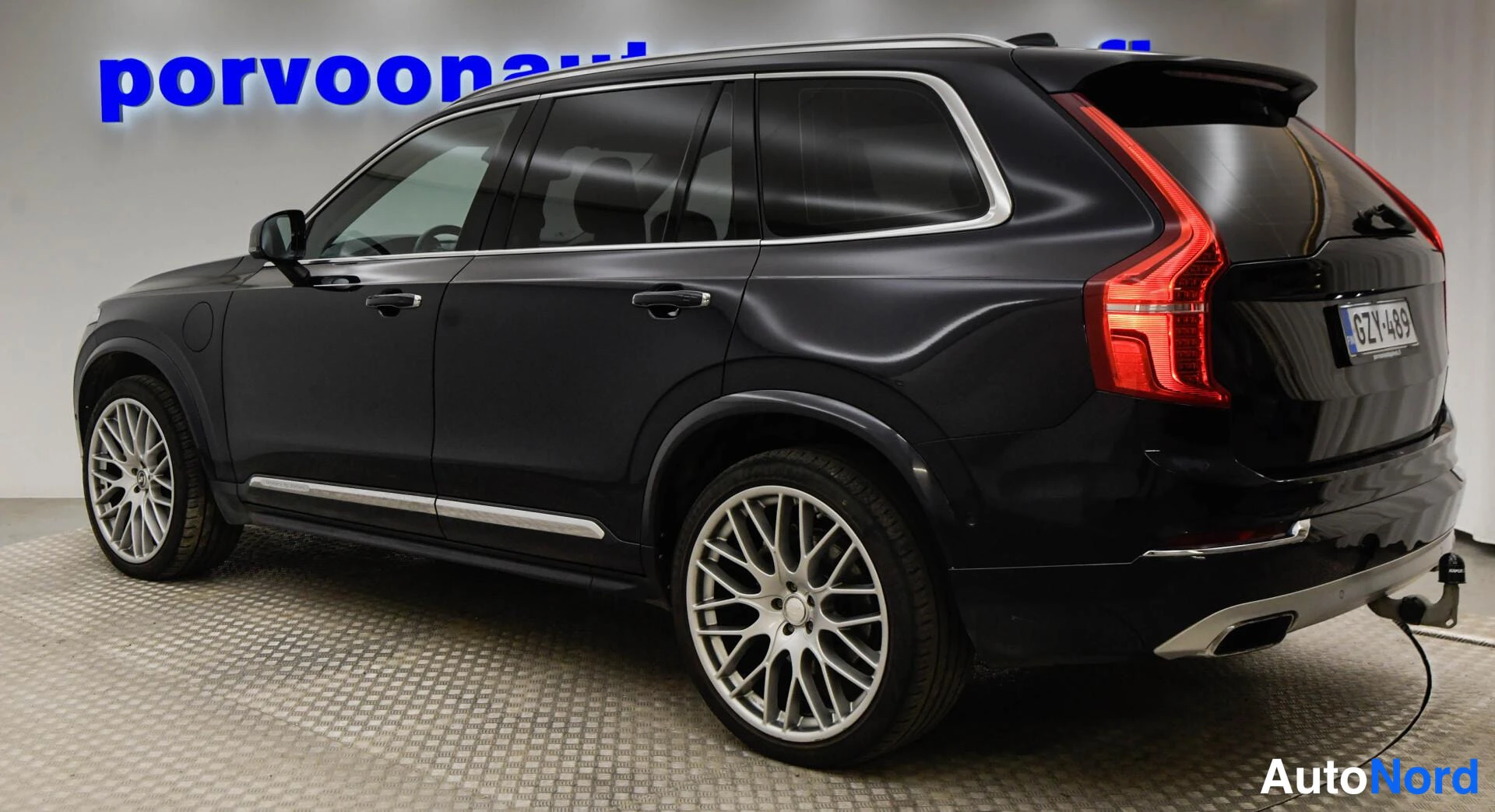 Takaviisto: Takanurkkanäkymä tummasta Volvo XC90 -maasturista, rekisterikilpi ja punaiset takavalot näkyvissä.