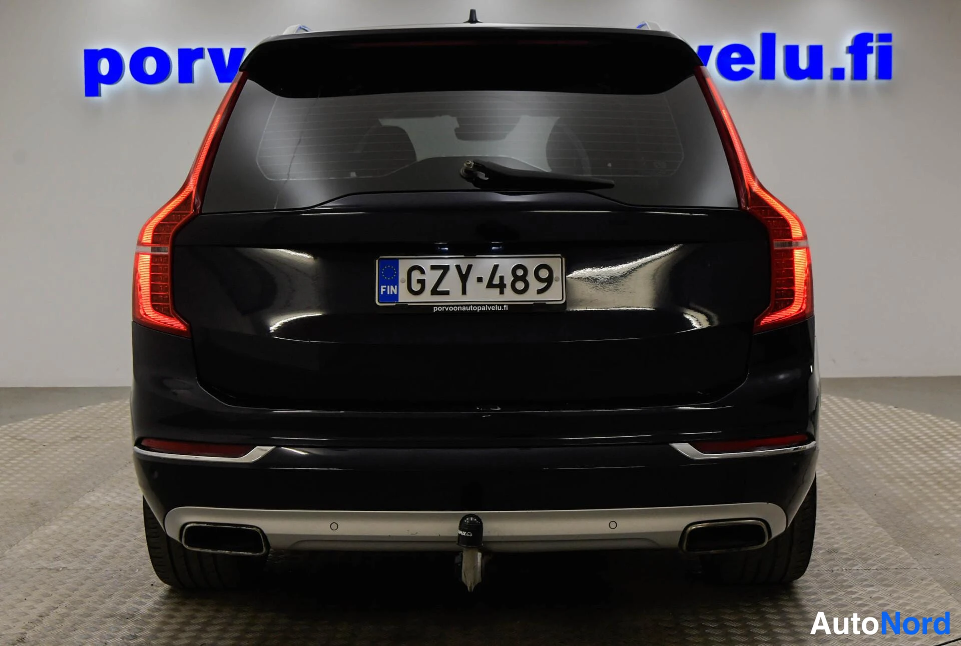 Takaa: Takaa kuvattu tumma Volvo XC90, rekisterikilpi, lieskat ja vetokoulu näkyvissä.