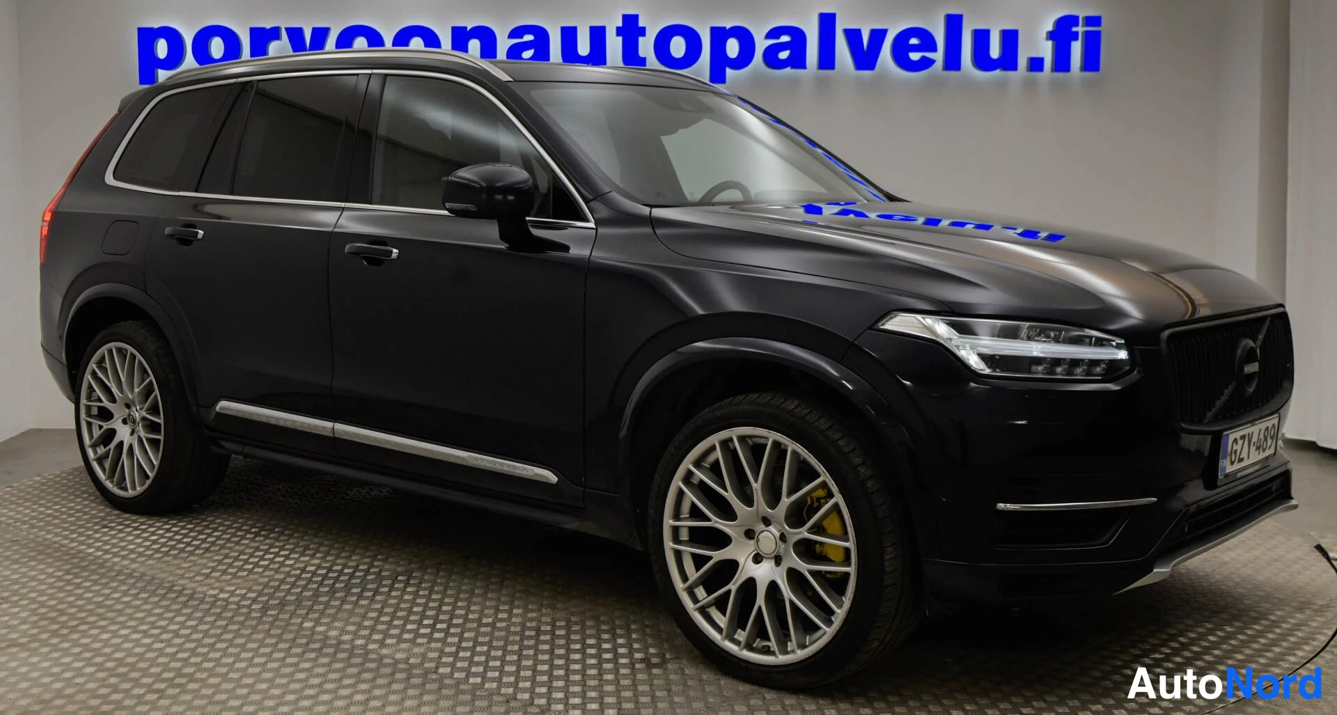 Etuviisto, nokka oikealle: Mustan tila-auton etukolmasosan näkymä: Volvo-merkki säleikössä, sumuvalot, -rekisterikilpi ja hopeiset kevytmetallivanteet.