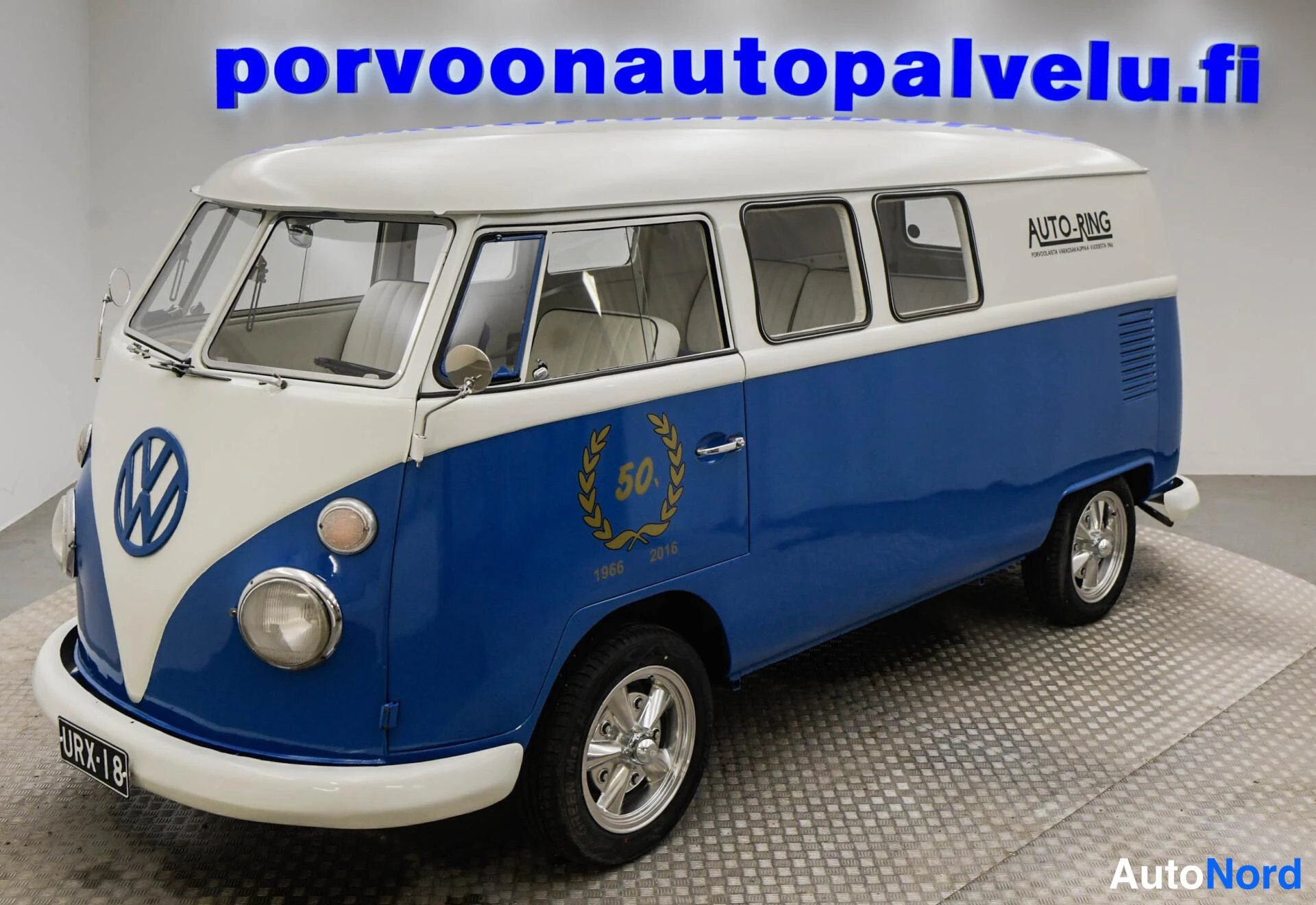 Etuviisto, nokka vasemmalle: Sinivalkoinen Volkswagen -pakettiauto etuviistossa, nokka vasemmalla.