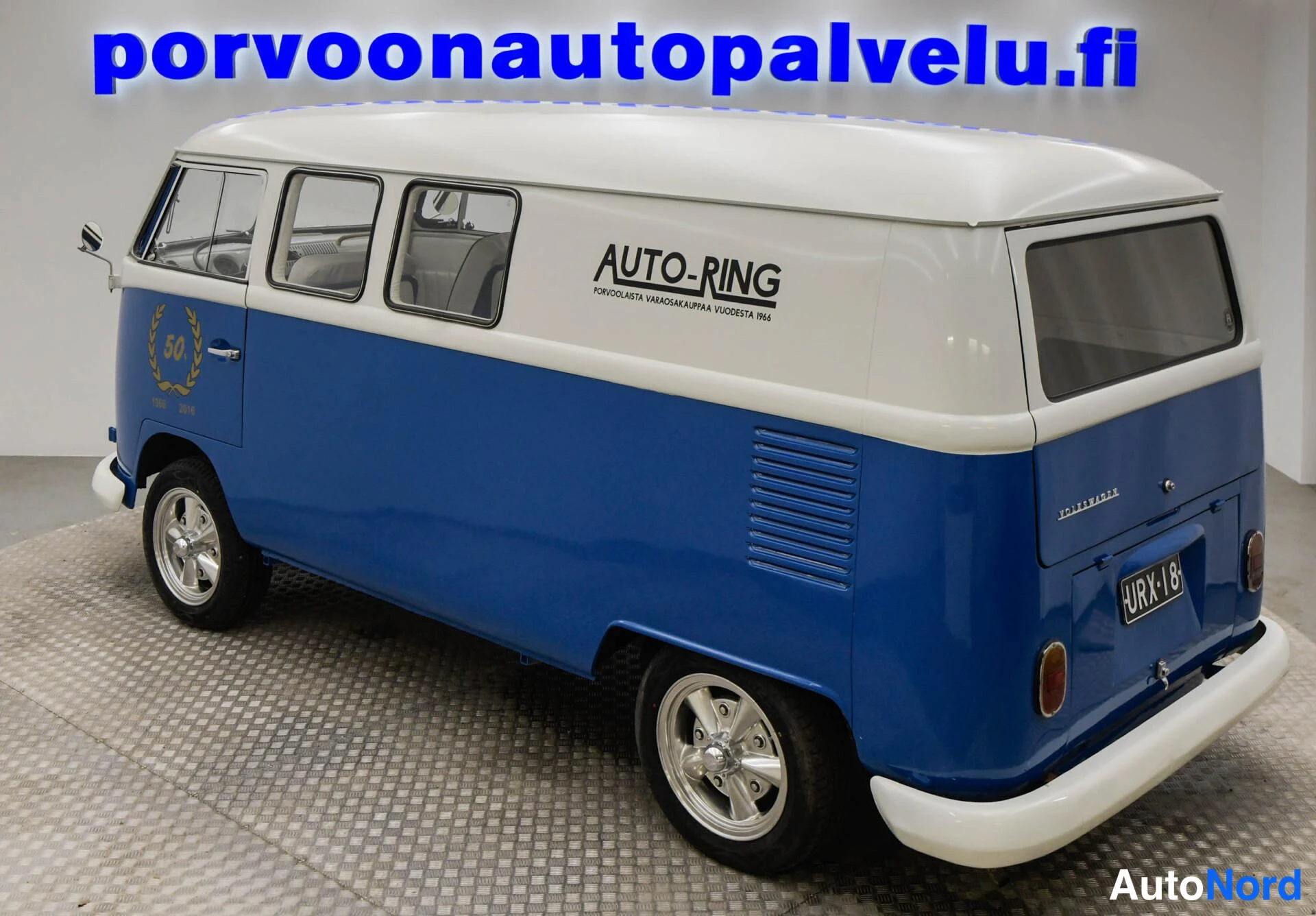 Takaviisto: Sinivalkoinen Volkswagen -pakettiauto takaviistossa, perä vasemmalla.