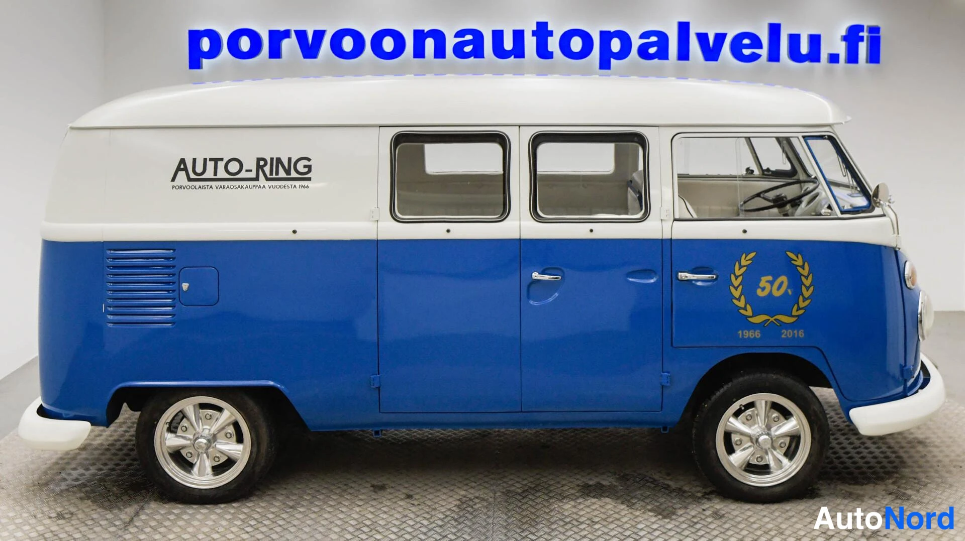 Sivulta: Pakettiauton sivuprofiili oikealta: sininen alaosa, valkoinen katto, Auto-Ring-mainos ja 50-vuotismerkintä ovessa.