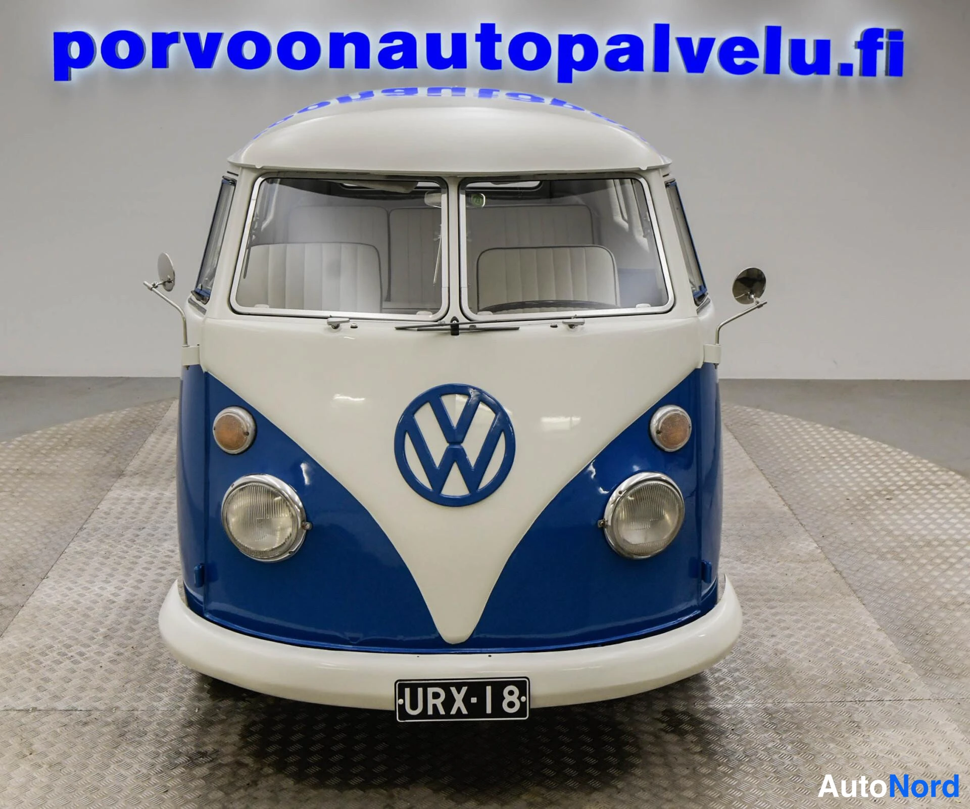 Edestä: Pakettiauton suora etunäkymä: kaksi ajovaloa, VW-logo ja rekisteritunnus.