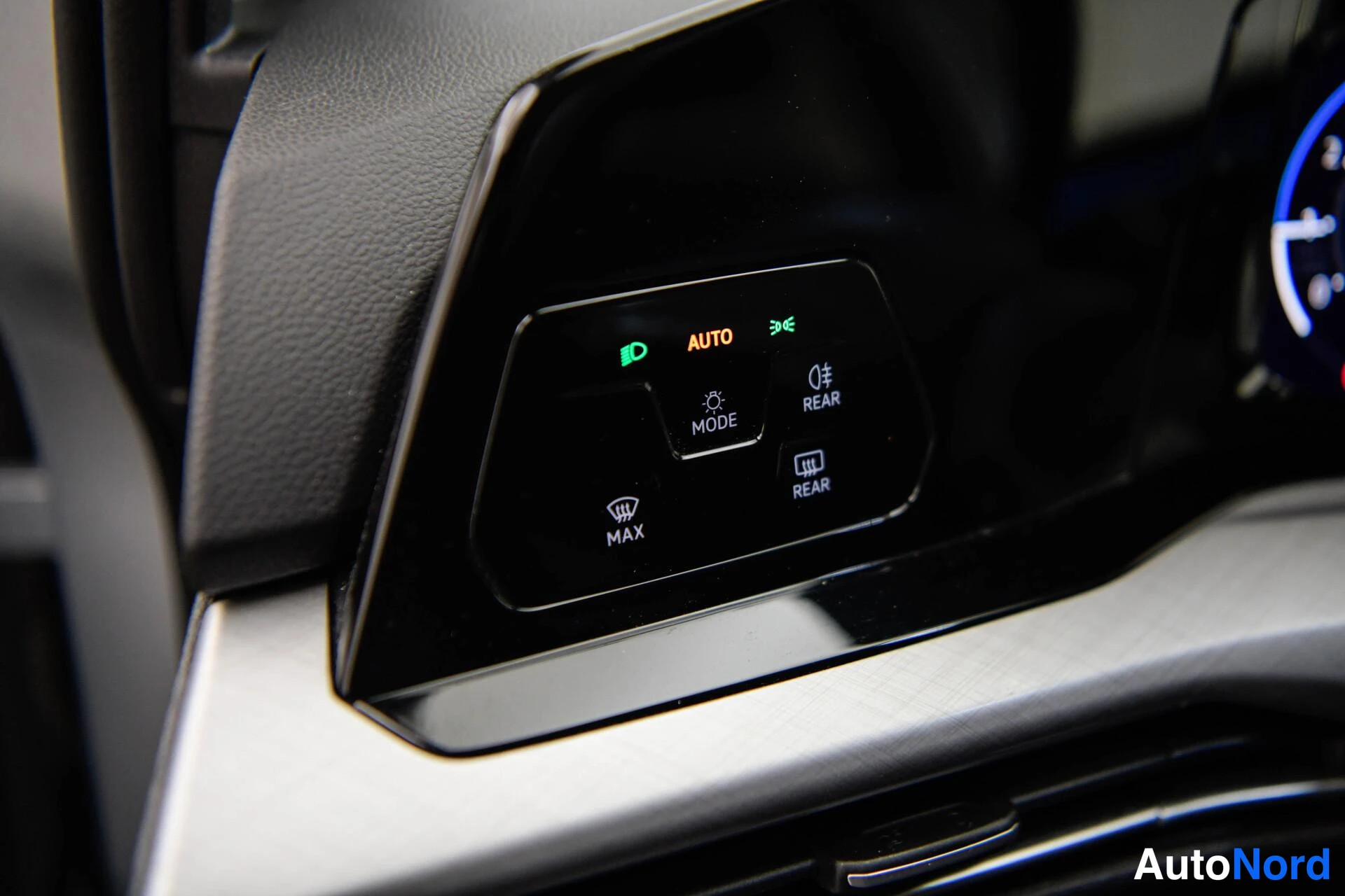 Yksityiskohta: Sisätilakuvan kohdennus auton ajovalojen ohjauskytkimestä, jossa näkyvät AUTO-, MODE-, MAX- ja REAR-merkit.