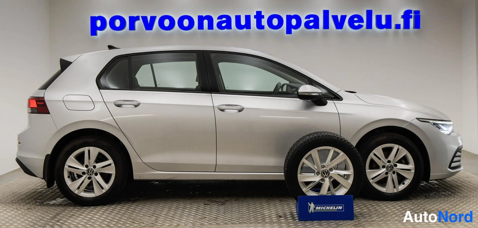 Etuviisto, nokka oikealle: Volkswagen Golf -henkilöauto sivulta oikealta, hopeanvärinen kori ja irrotettu lumirengas kuvassa.