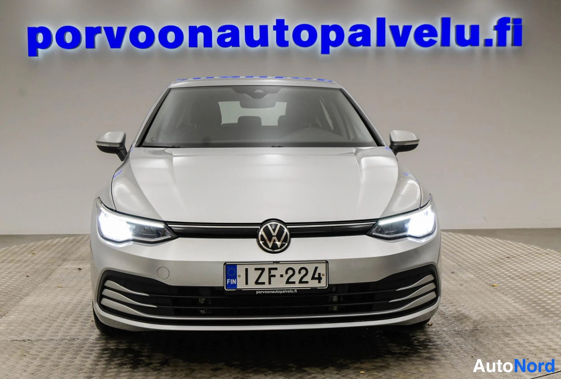 Edestä: Volkswagen Golf -henkilöauto suoraan edestä, hopeanvärinen kori, rekisterikilpi.