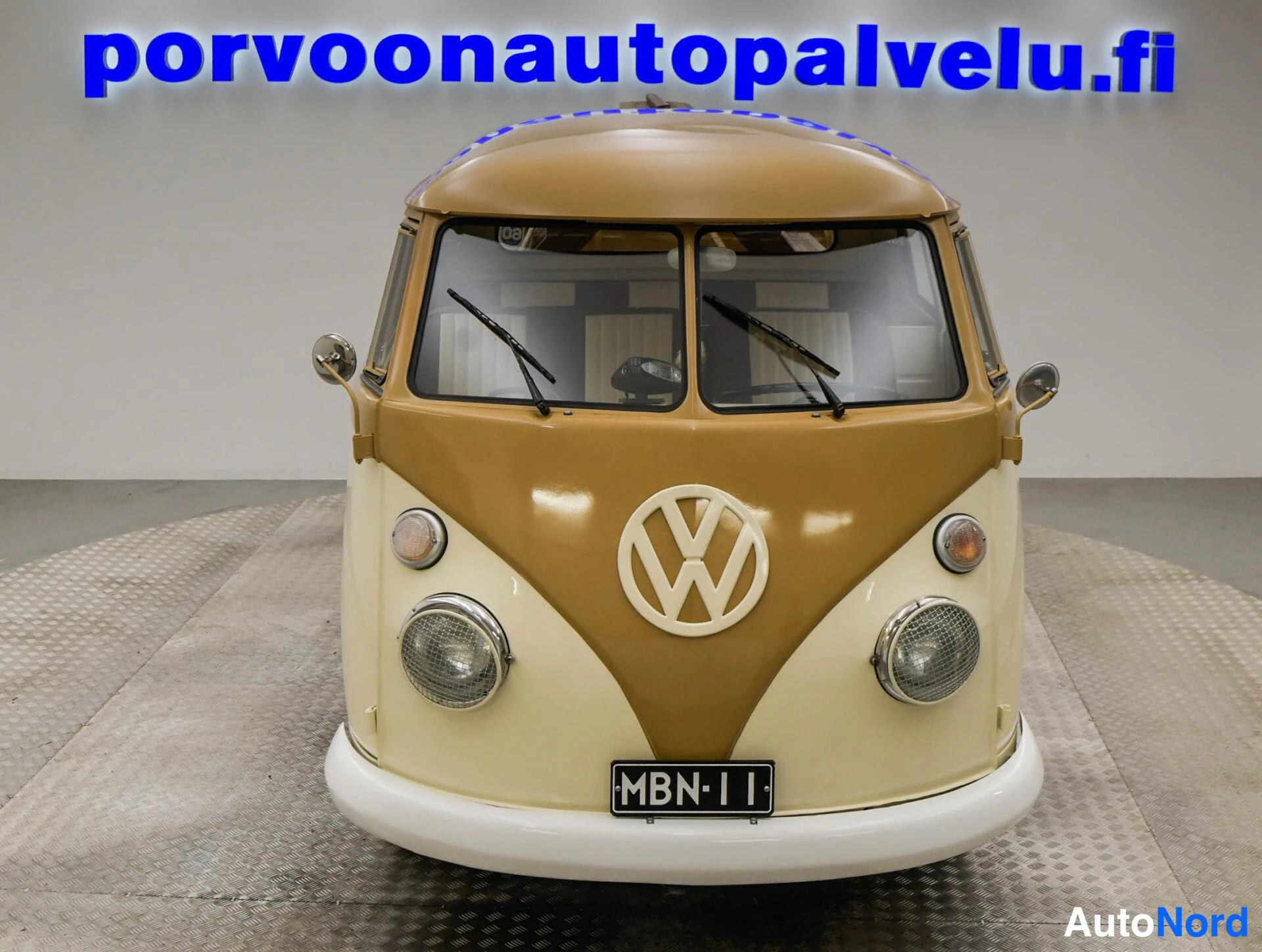 Edestä: Suora etukuva Volkswagenin konepellistä; pyöreät ajovalot, VW-merkki ja rekisterikilpi.