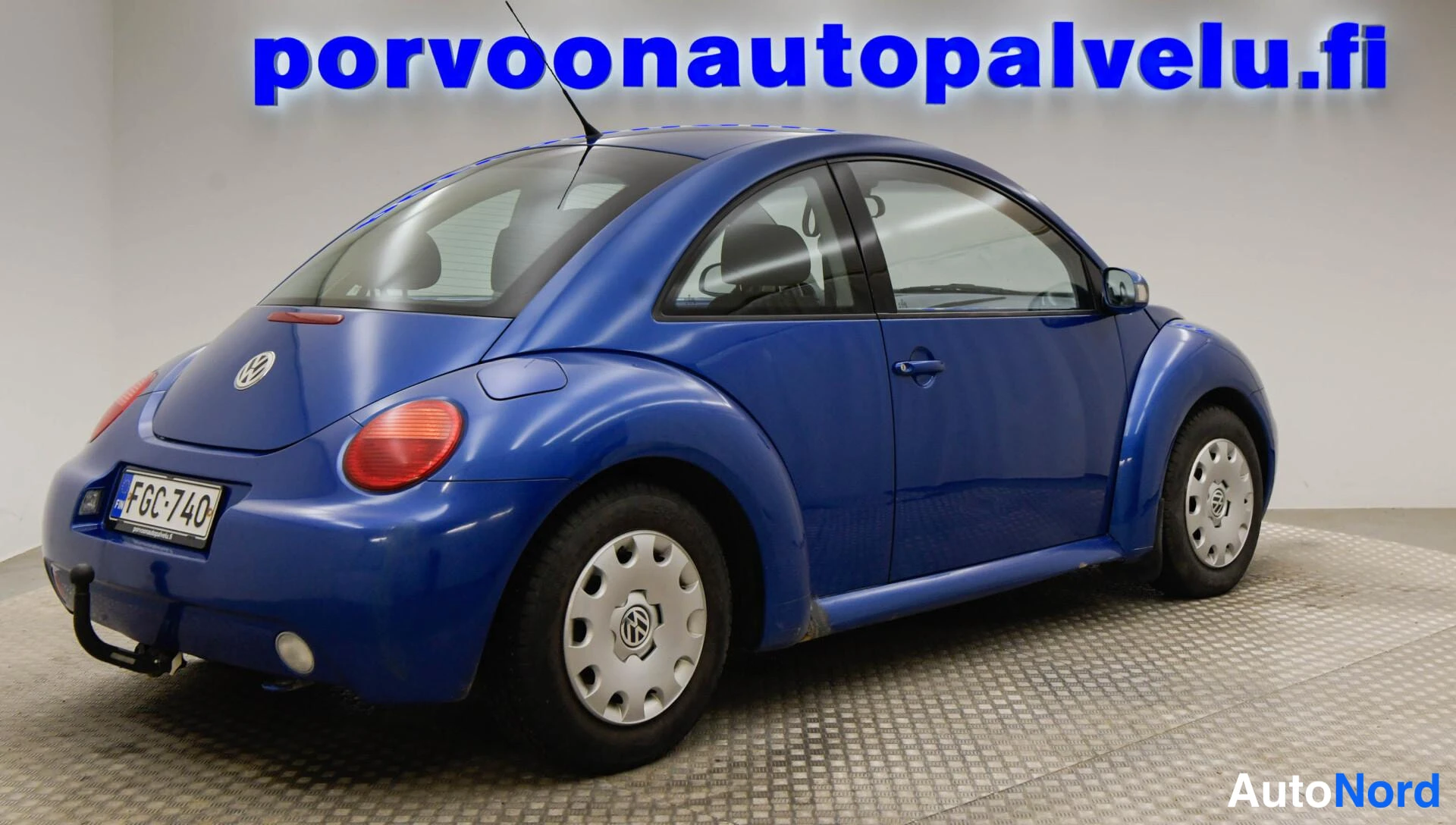 Takaviisto: Sininen Volkswagen New Beetle takakulmakuva toisesta suunnasta, rekisterikilpi.