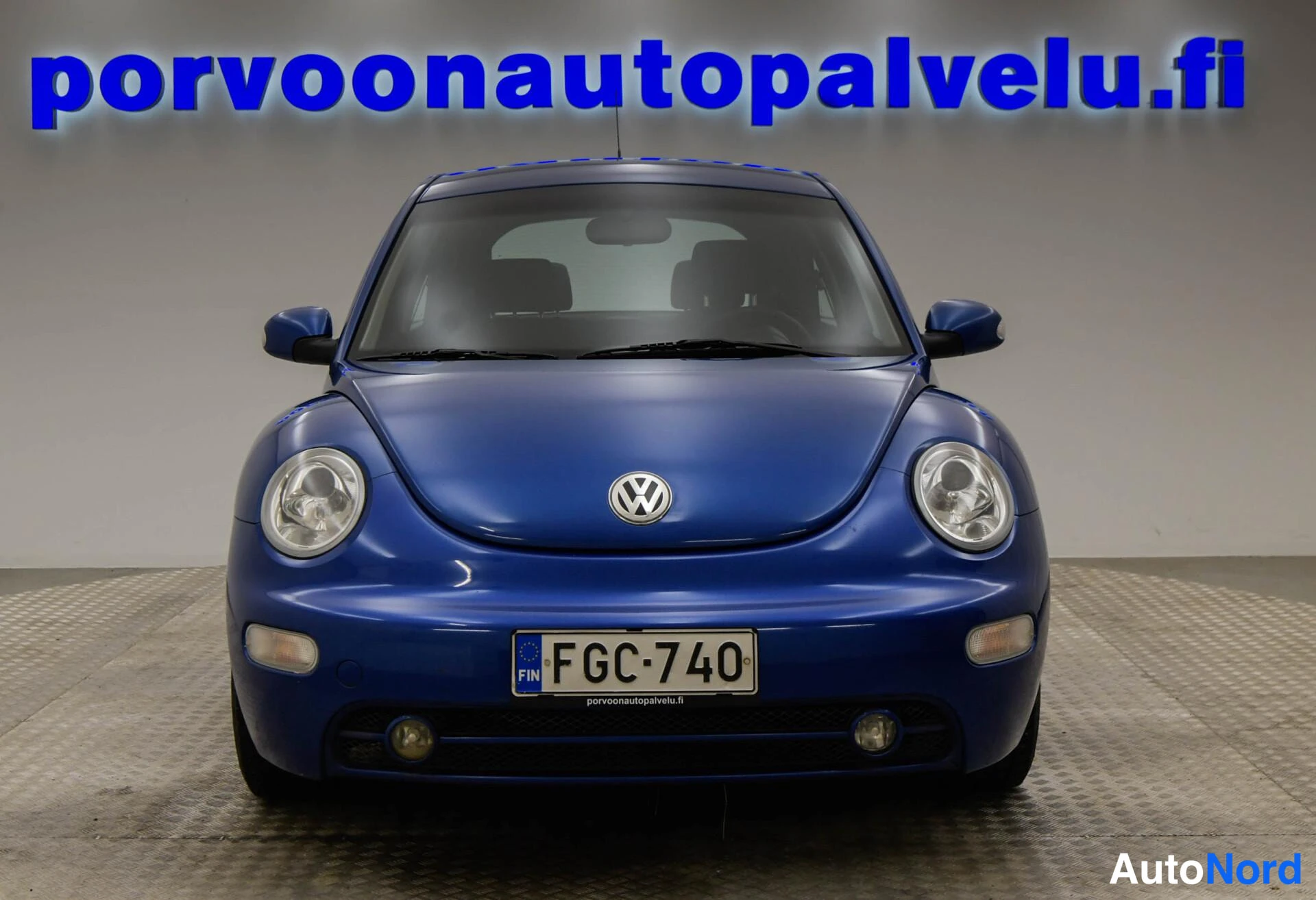 Edestä: Sinisen Volkswagen New Beetlen etupää suoraan edestä, rekisterikilpi.