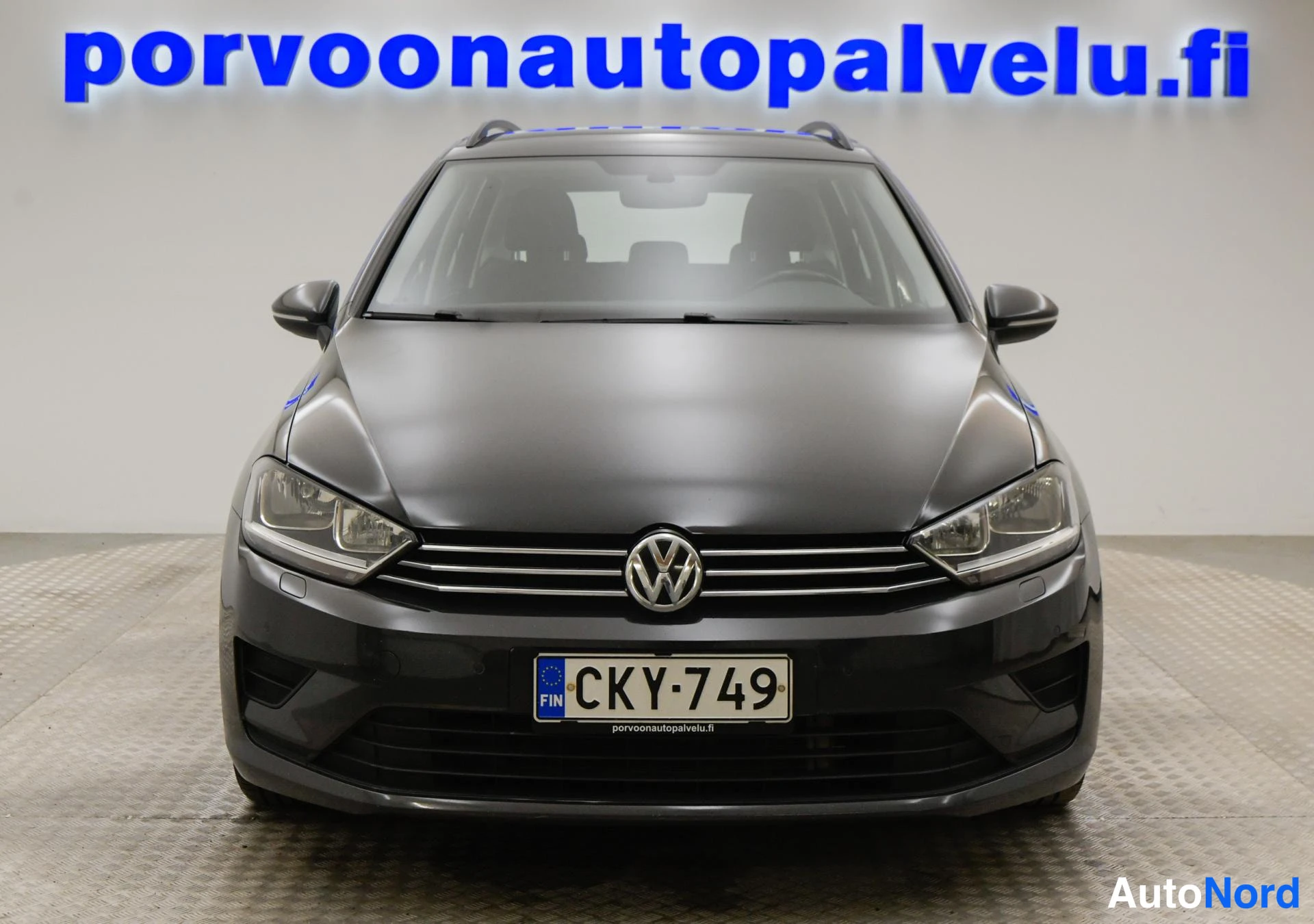 Edestä: Etukulmakuva Volkswagen Golf Sportsvanista; tummanharmaa keula, VW-merkki, sumuvalot ja rekisteritunnus FIN-merkinnällä.