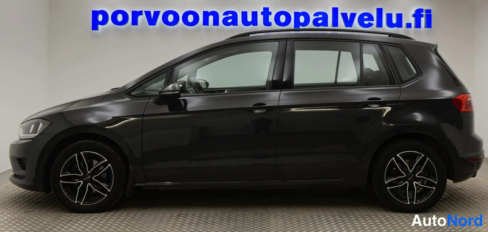 Takaviisto: Sivukulmakuvassa Volkswagen Golf Sportsvanin vasen kylki ja takaosa; tummanharmaa korimaali, kattokaiteet ja mustat moniväriset vanteet.